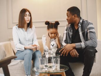 Two parents discussing custody issues with a distraught child on the couch