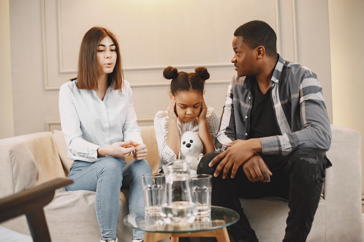 Two parents discussing custody issues with a distraught child on the couch