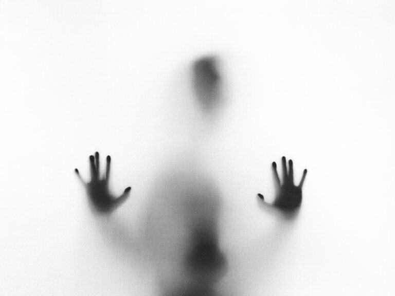 Shadowy figure behind glass with hands pressed against the surface