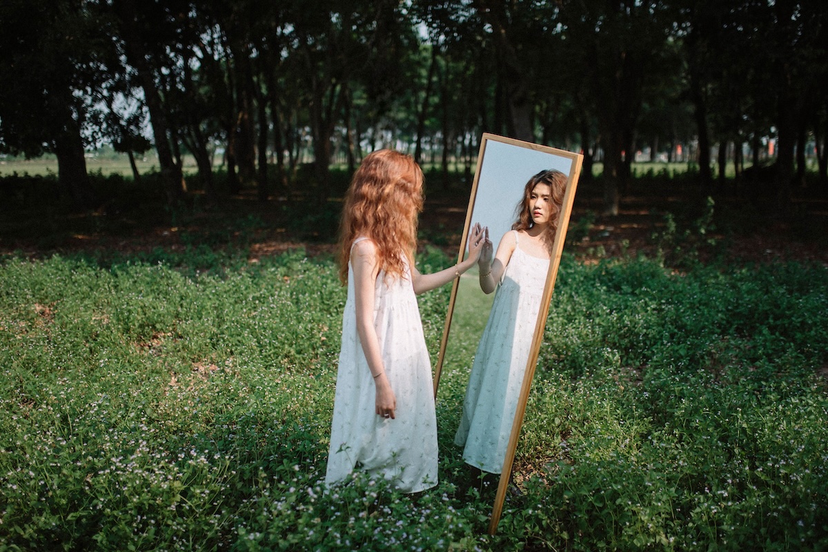 Woman standing before a mirror in a wooded setting, reflecting the relationship between therapist and patient.