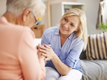 Middle-aged caregiver holding the hands of an elderly woman