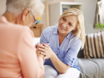 Middle-aged caregiver holding the hands of an elderly woman