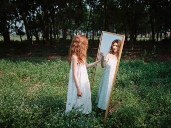 Woman standing before a mirror in a wooded setting, reflecting the relationship between therapist and patient.